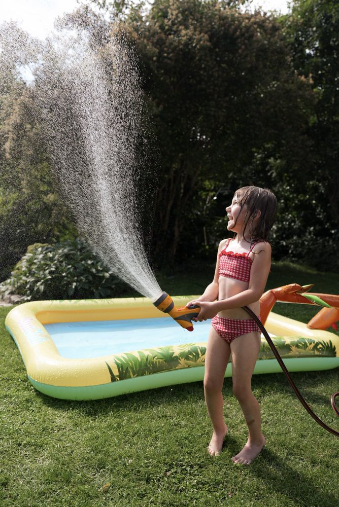 A little girl spraying the hose over a backyard pool